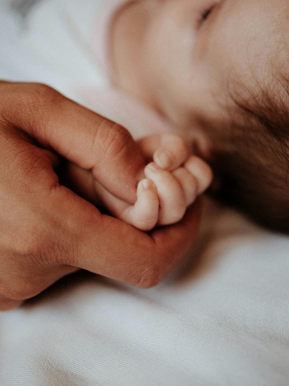 A parent's hand holding a sleeping newborn's hand