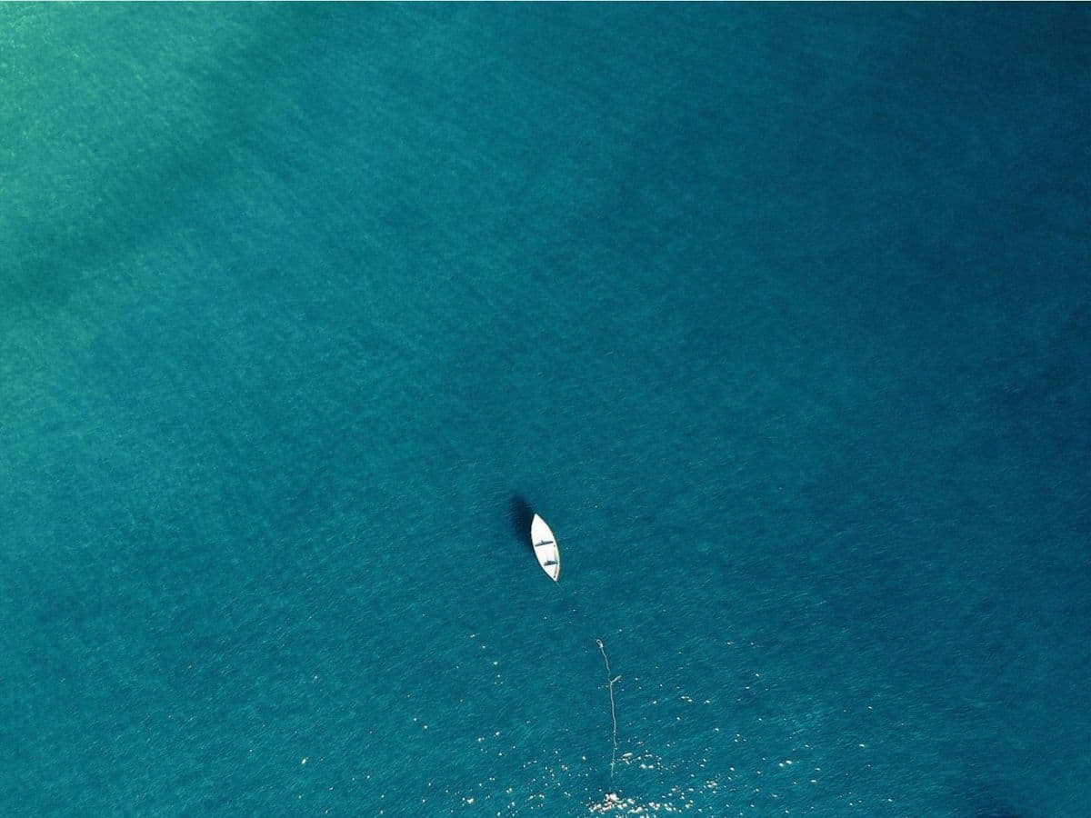 A small white boat at rest on calm turquoise water, seen from above